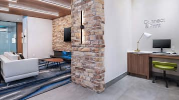 A modern office space with a stone accent wall, a flat-screen TV, a desk with a computer, and a comfortable seating area with a sofa and a coffee table.