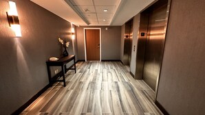 A hallway with a wooden floor, a desk with a vase, and two elevators. - Fairfield by Marriott Inn & Suites Newmarket (Newmarket)