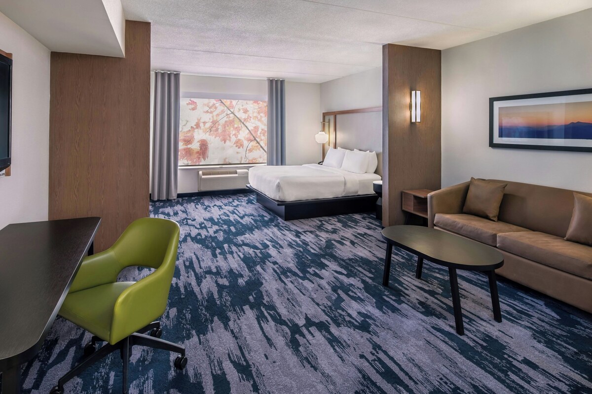 Une chambre d’hôtel avec un lit, une chaise verte, un canapé marron, une petite table et un tableau au mur.