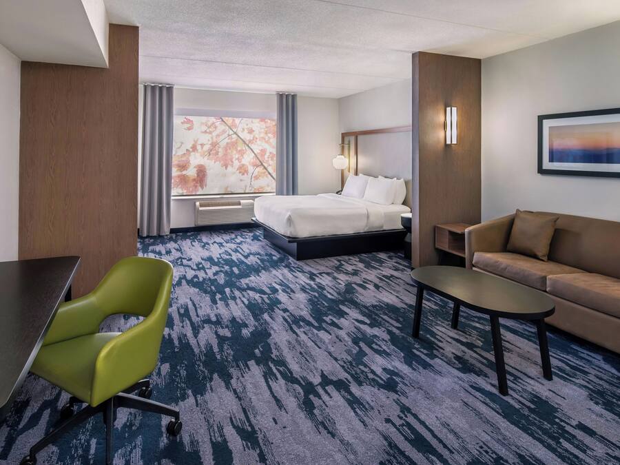 Una habitación de hotel con una cama, una silla verde, un sofá marrón, una mesita y un cuadro en la pared.