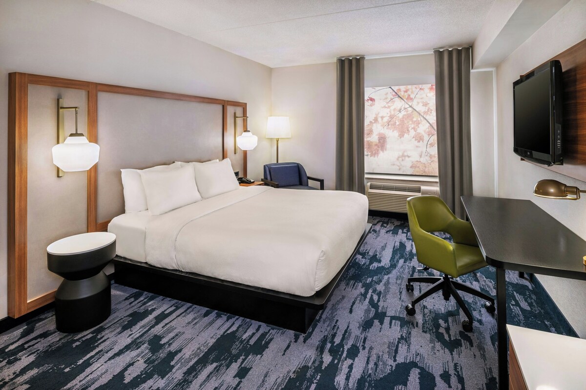 Une chambre d’hôtel équipée d’un lit, de lampes de chevet, d’un bureau, d’une chaise, d’une télévision et d’une fenêtre avec des rideaux.