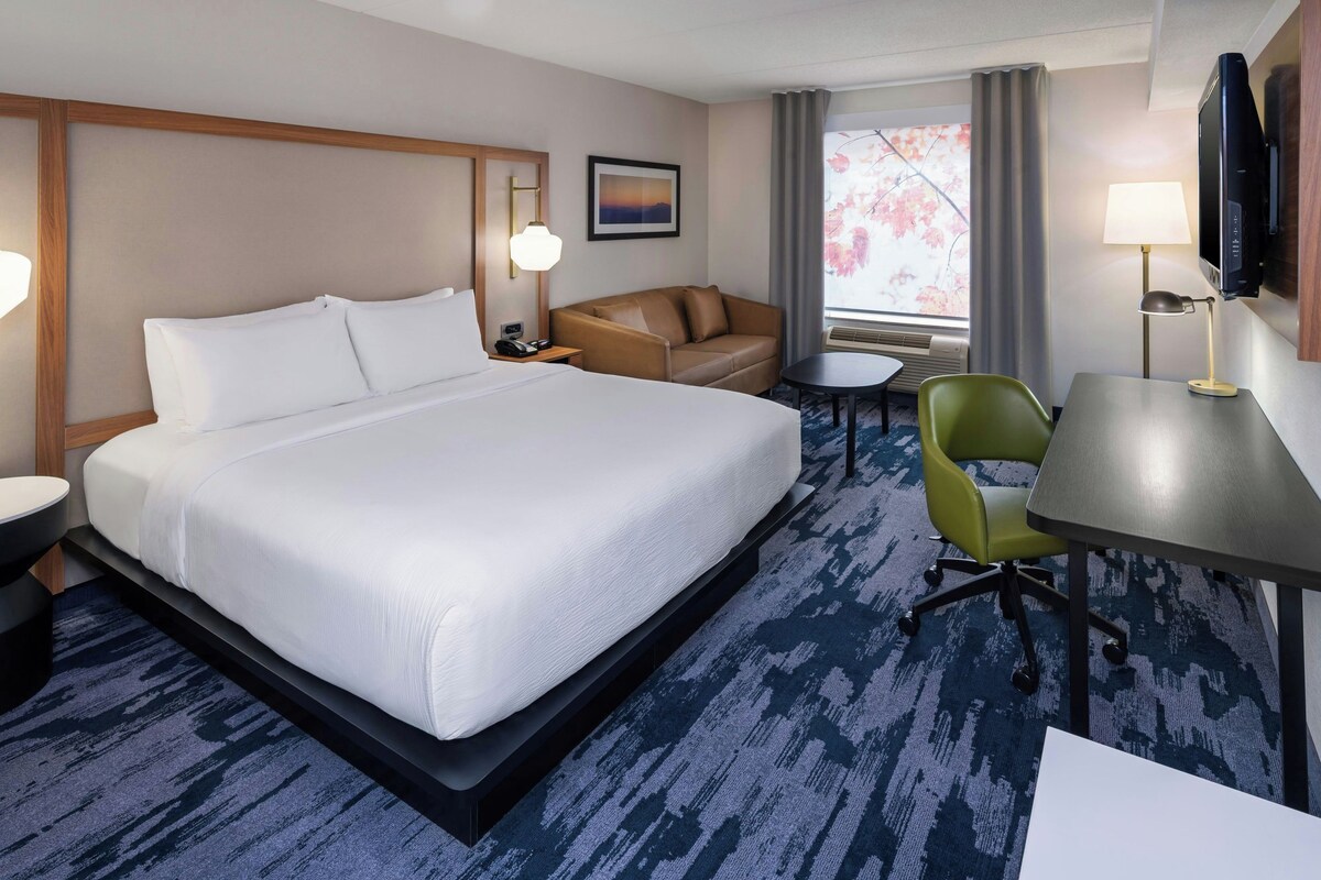 Une chambre d’hôtel avec un grand lit, un canapé, un bureau, une chaise, une télévision et une fenêtre avec des rideaux.