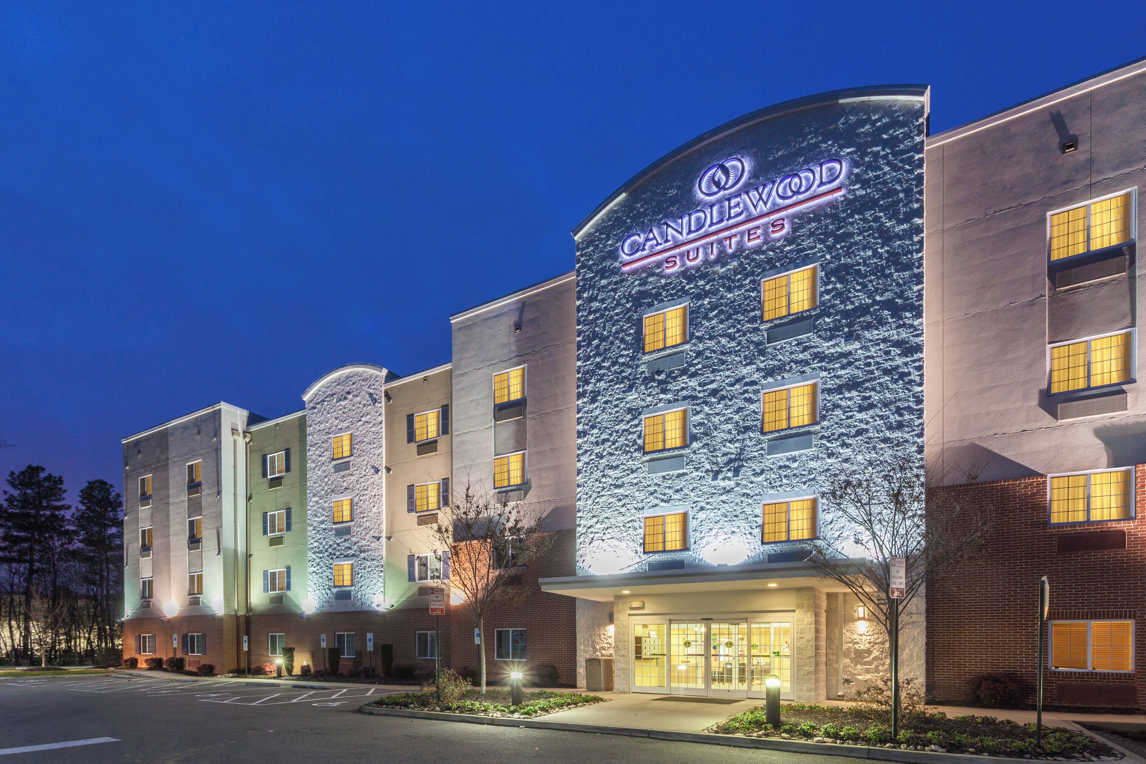 A hotel with multiple stories, a prominent sign for Candlewood Suites, and a parking lot in front.
