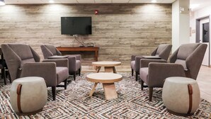 Un salón de conferencias con cuatro sillas grises, dos mesas redondas, un televisor de pantalla plana montado en una pared de madera y una alfombra estampada.