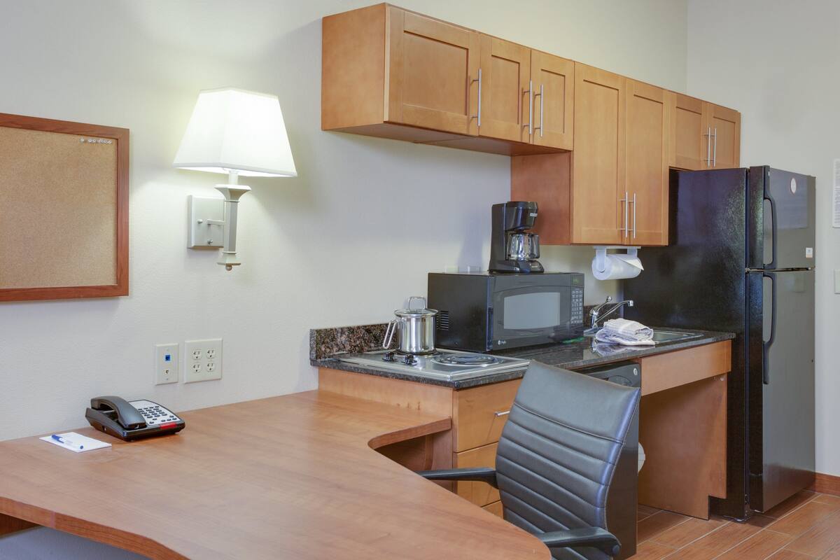 A compact kitchen with wooden cabinets, a microwave, a coffee maker, and a refrigerator.