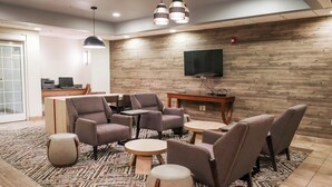 Un espacio lounge moderno con sofás, mesas y un televisor de pantalla plana montado en la pared.