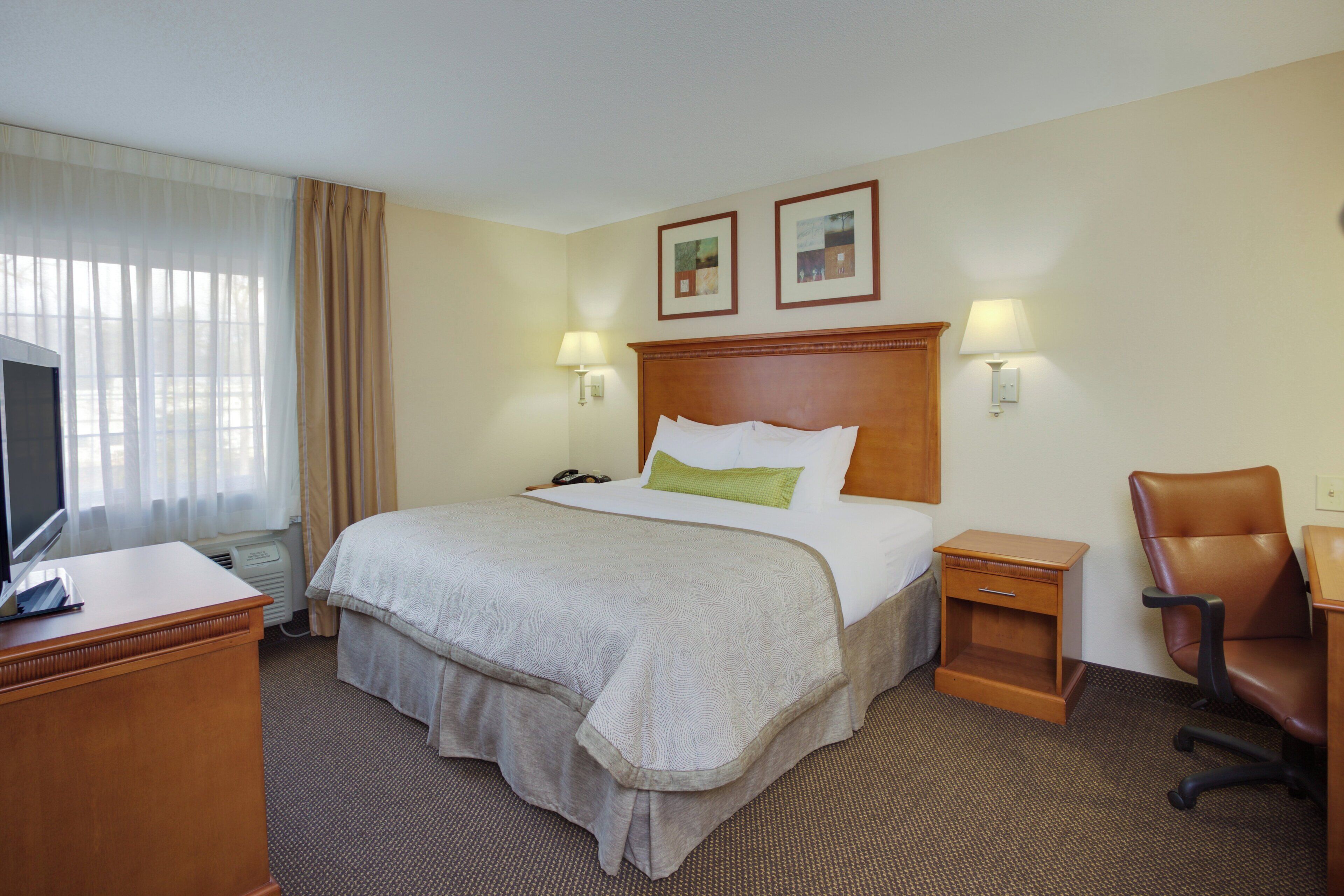 A hotel room with a bed, a desk, a chair, a television, and two wall-mounted lamps.