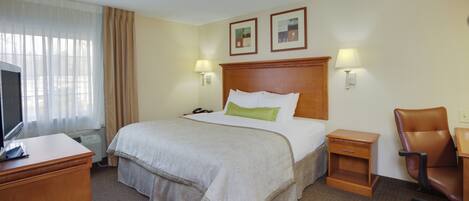 A hotel room with a bed, a desk, a chair, a television, and two wall-mounted lamps.