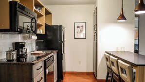 Cocina compacta con microondas, cafetera y refrigerador. Zona de comedor con mesa y sillas.