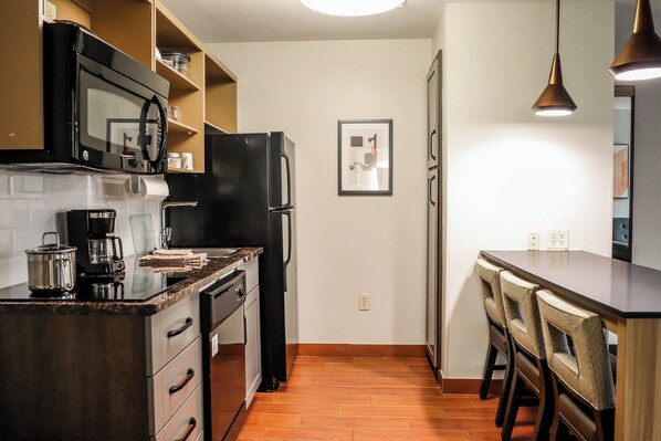 Cocina compacta con microondas, cafetera y refrigerador. Zona de comedor con mesa y sillas.
