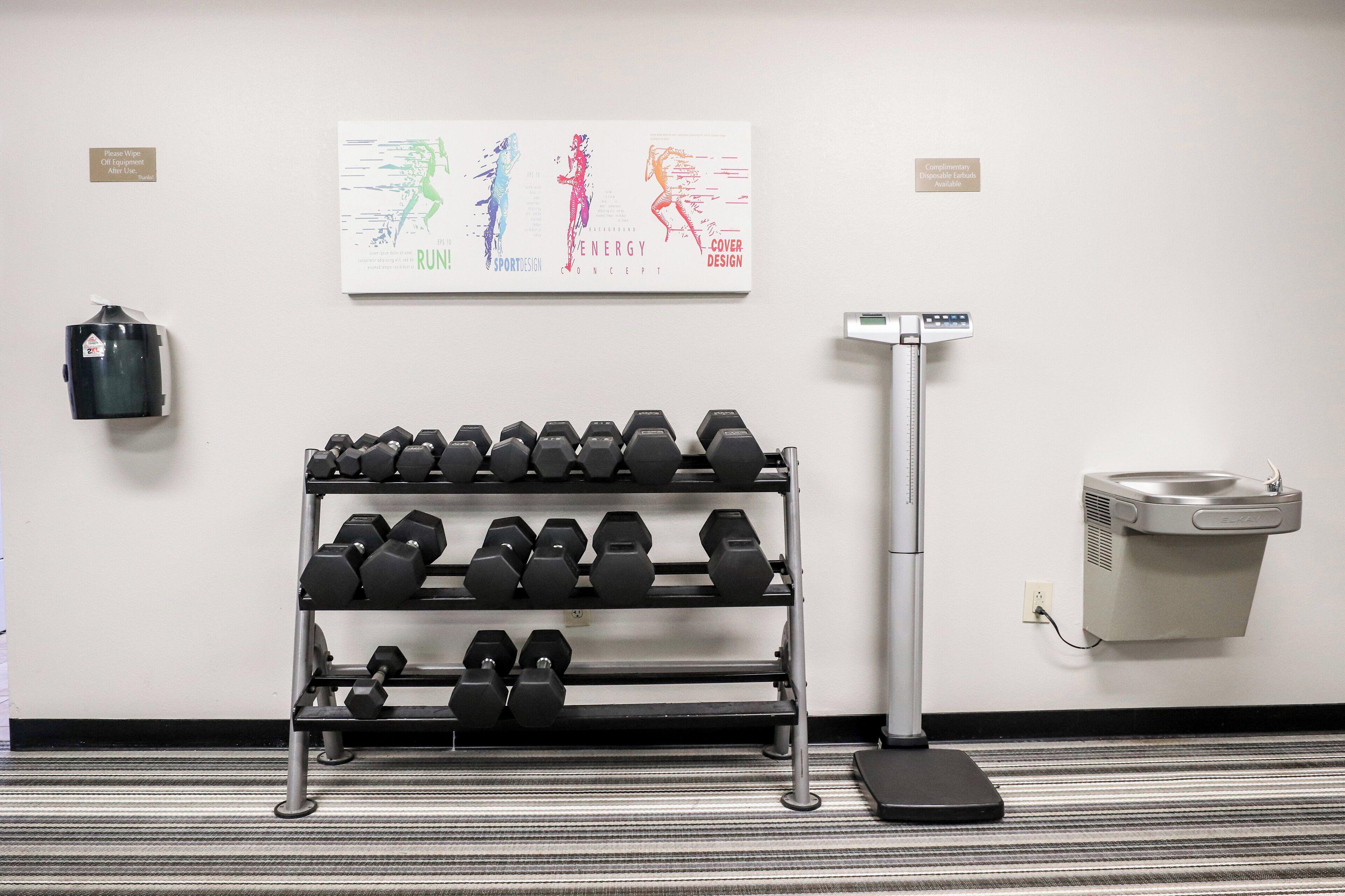 A gym with dumbbells on a rack, a scale, and a wall-mounted air purifier.