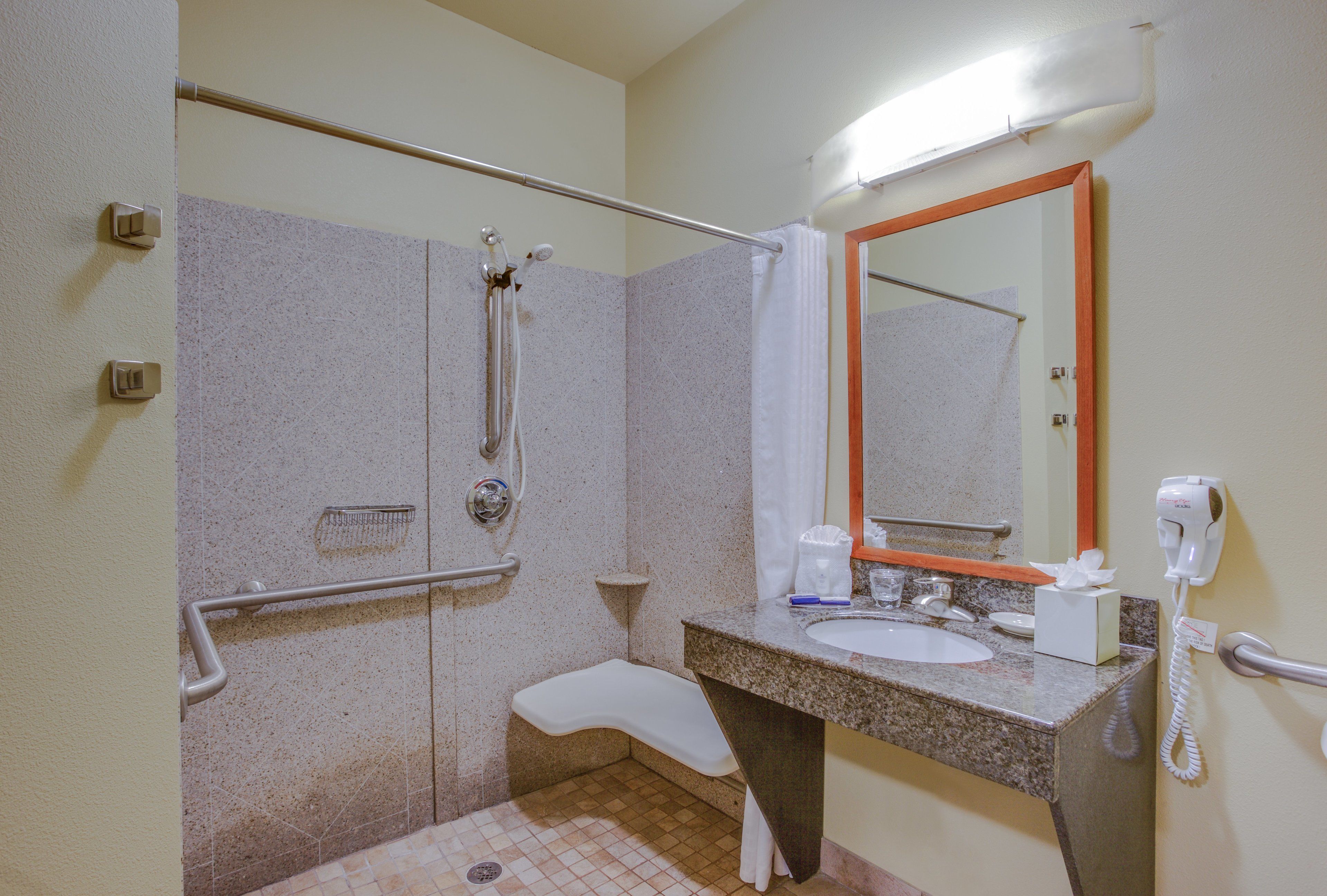 A bathroom with a shower, grab bar, sink, and a hairdryer.