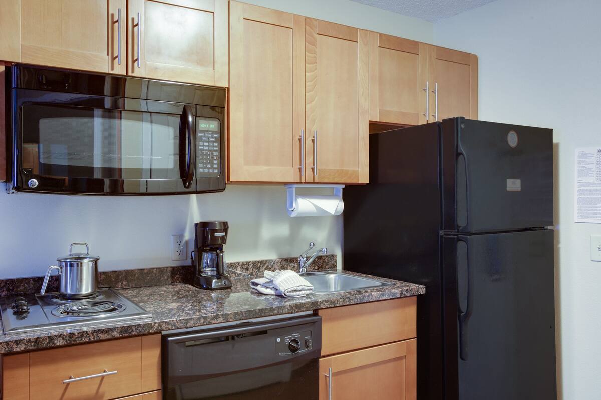 A kitchen with wooden cabinets, a black microwave, a black refrigerator, a stove, and a dishwasher.