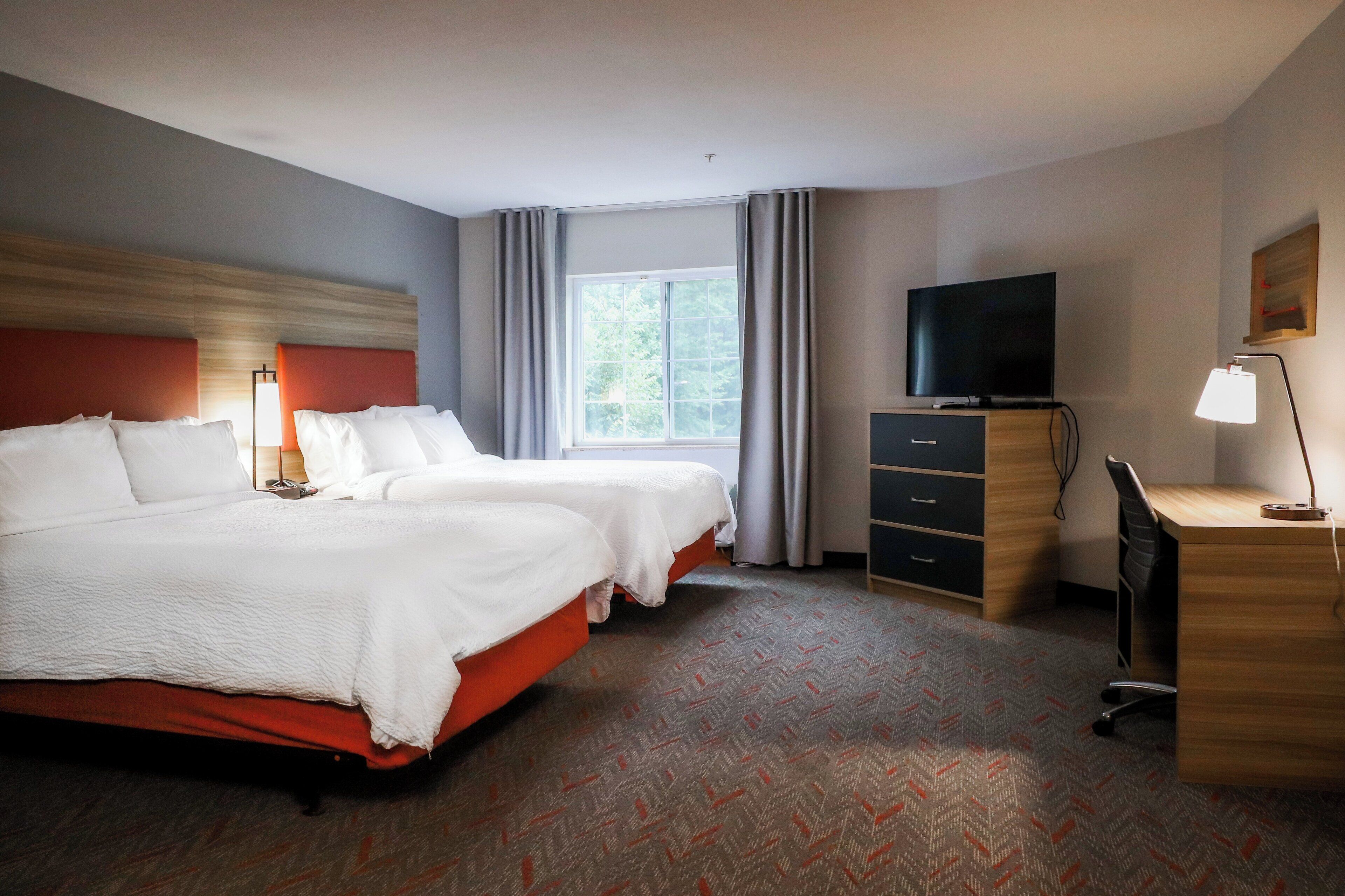 Une chambre d’hôtel avec deux lits, un bureau, une télévision et une fenêtre avec des rideaux.