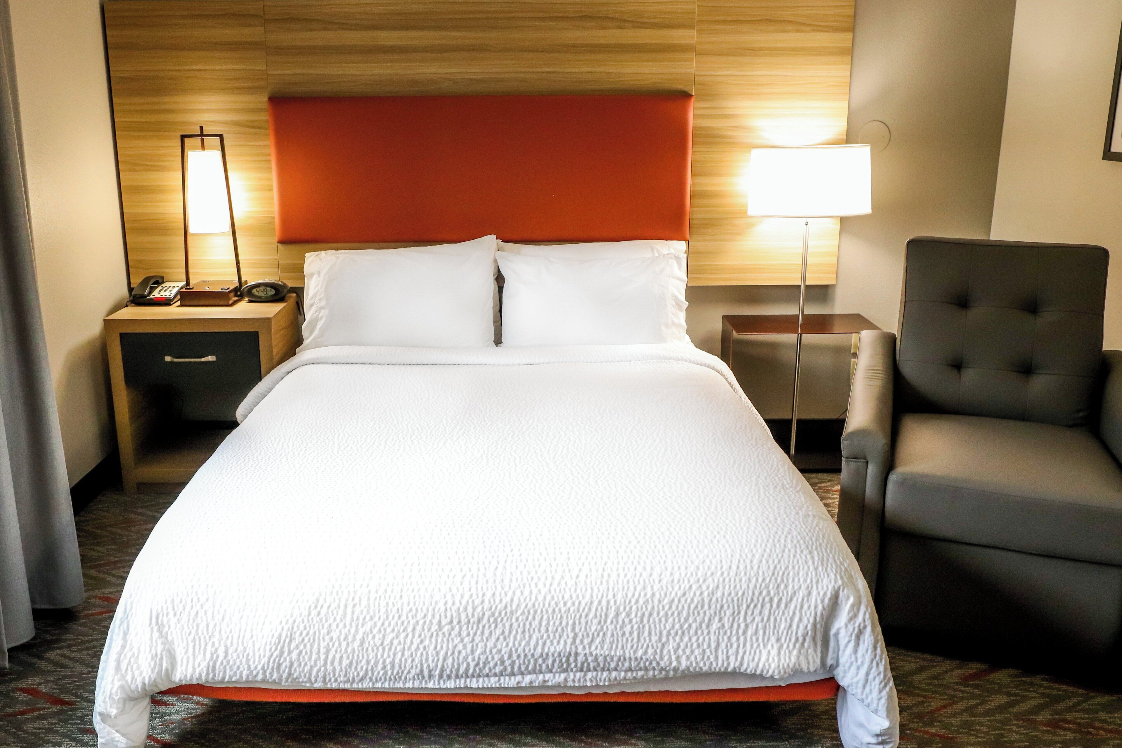 Une chambre d’hôtel avec un grand lit, une table de chevet avec un téléphone, une chaise et une lampe.