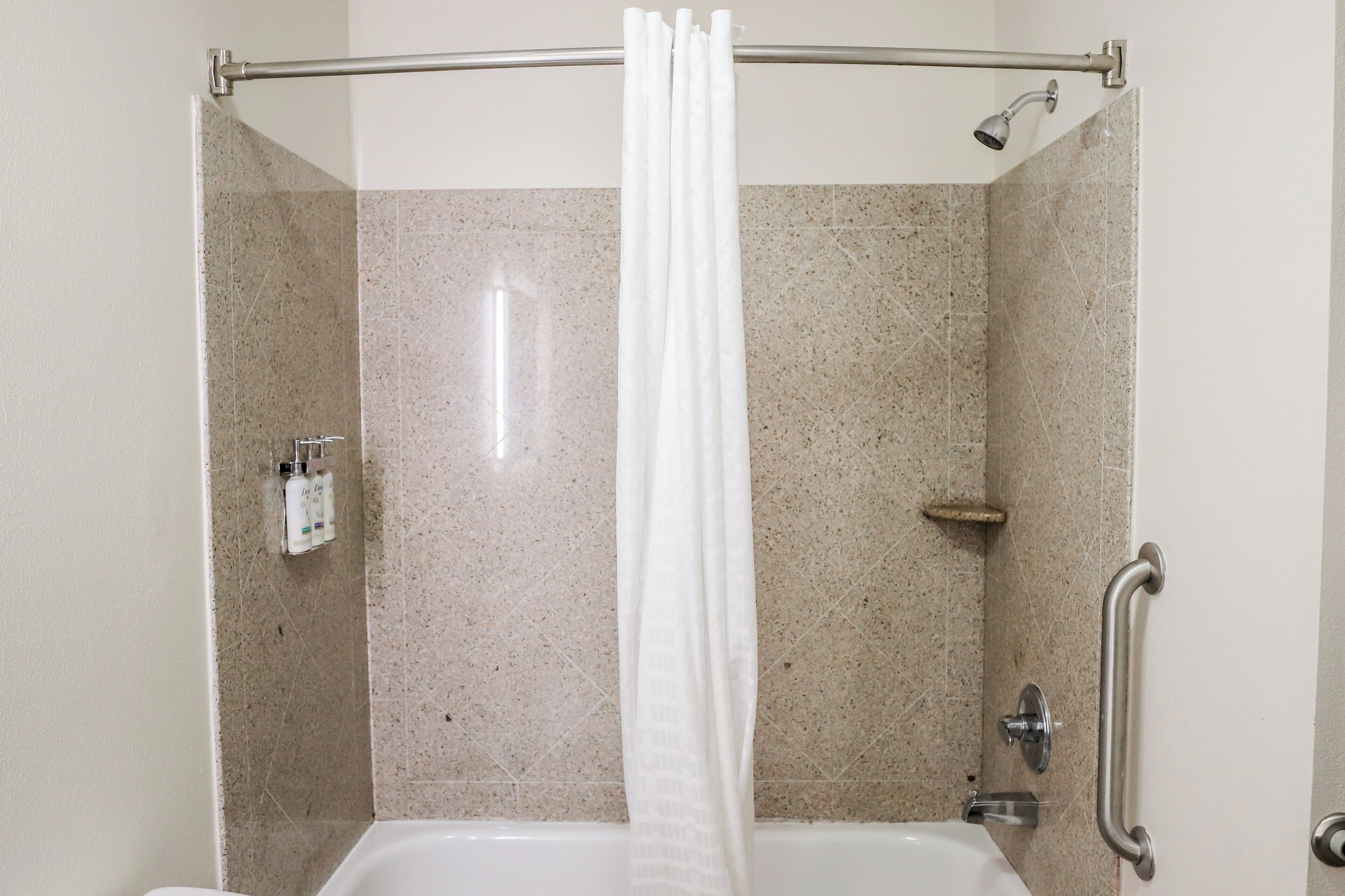 A shower area with a showerhead, a handrail, and a curtain.