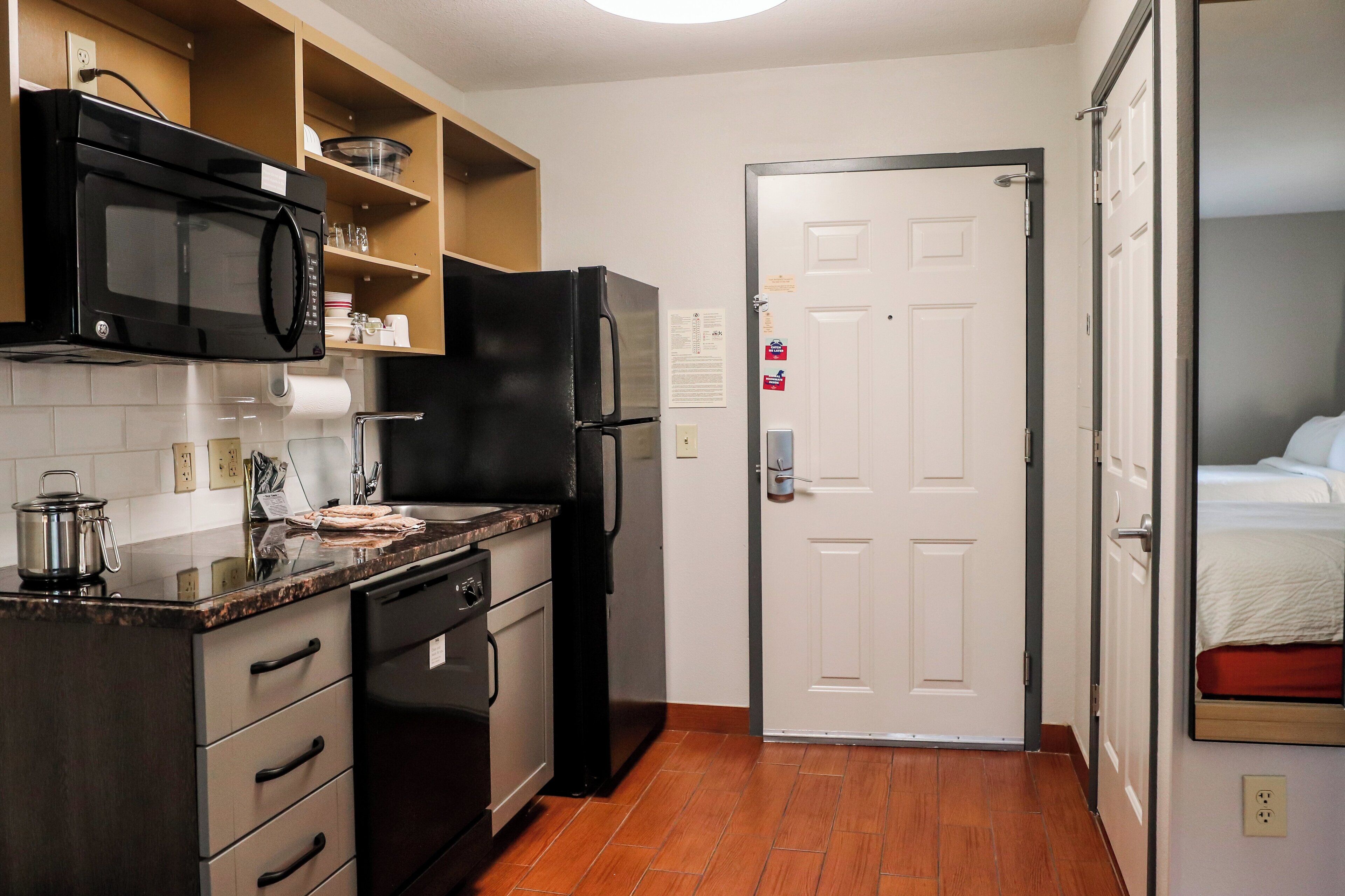 A compact kitchen with a microwave, stove, refrigerator, and wooden shelves.