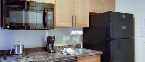 Une cuisine avec des meubles de rangement en bois, un réfrigérateur noir, un four à micro-ondes, une machine à café et un lave-vaisselle.