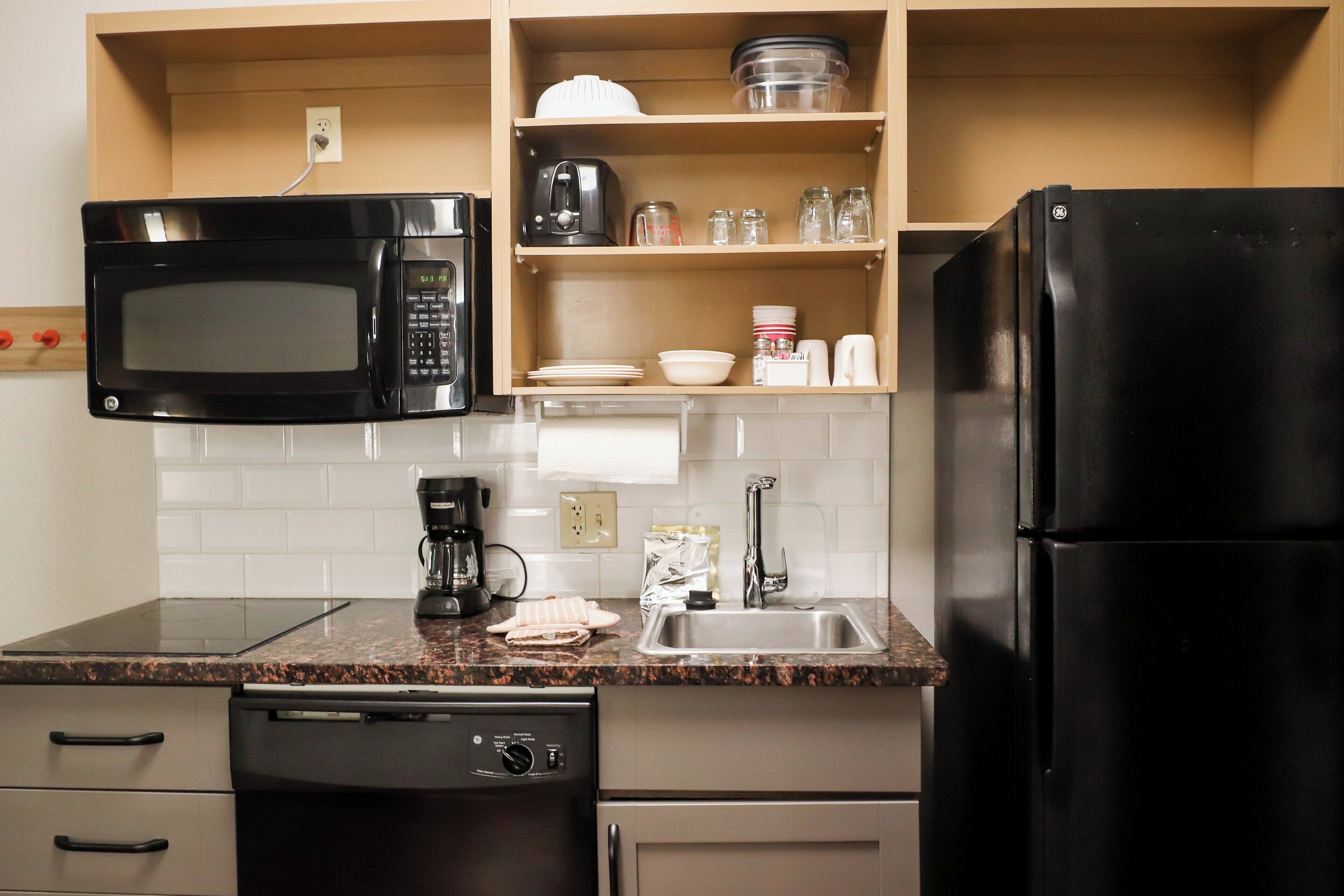 Een functionele keuken met een magnetron, koffiezetapparaat, spoelbak en vaatwasser.