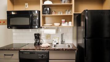 Een functionele keuken met een magnetron, koffiezetapparaat, spoelbak en vaatwasser.