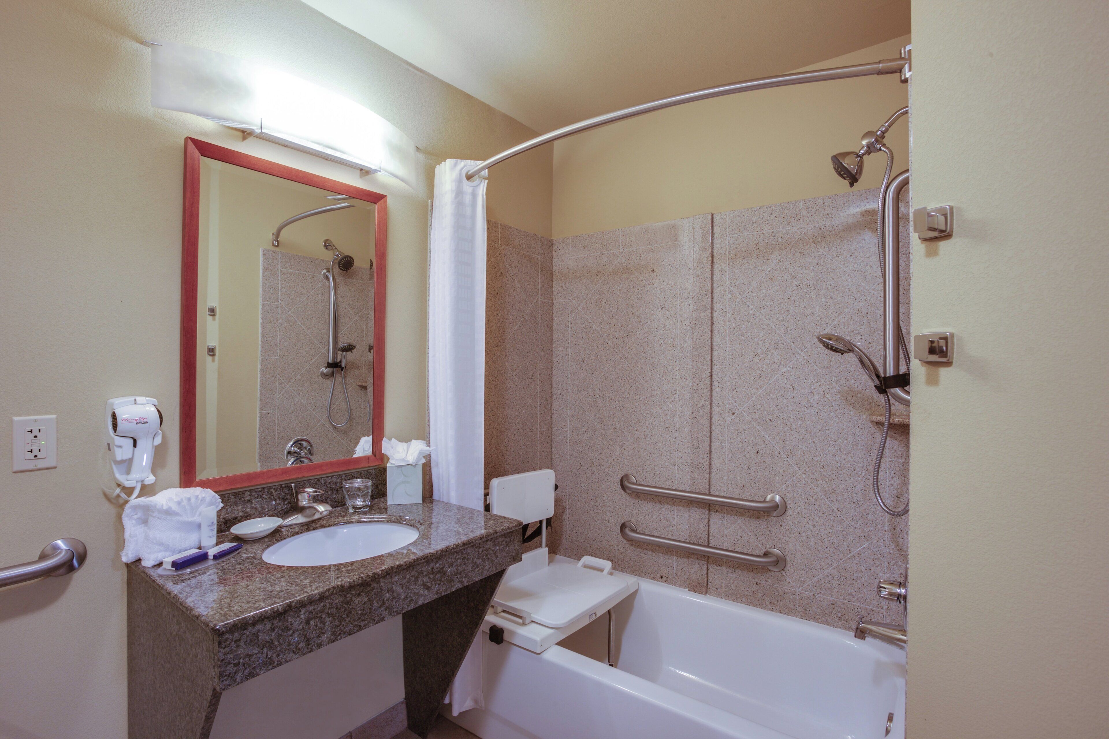 A bathroom with a sink, mirror, towel rack, shower, and grab bars.
