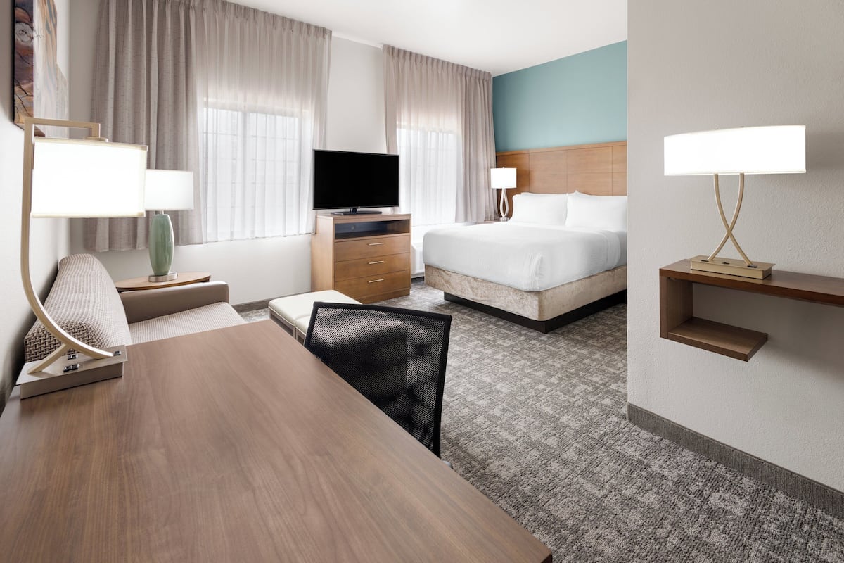 Een hotelkamer met een houten bureau, een televisie, een bed en een nachtkastje met een lamp.