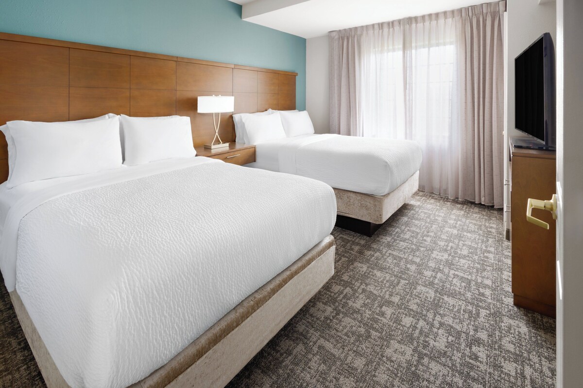 A hotel room with two beds, a wooden headboard, a television, and a carpeted floor.