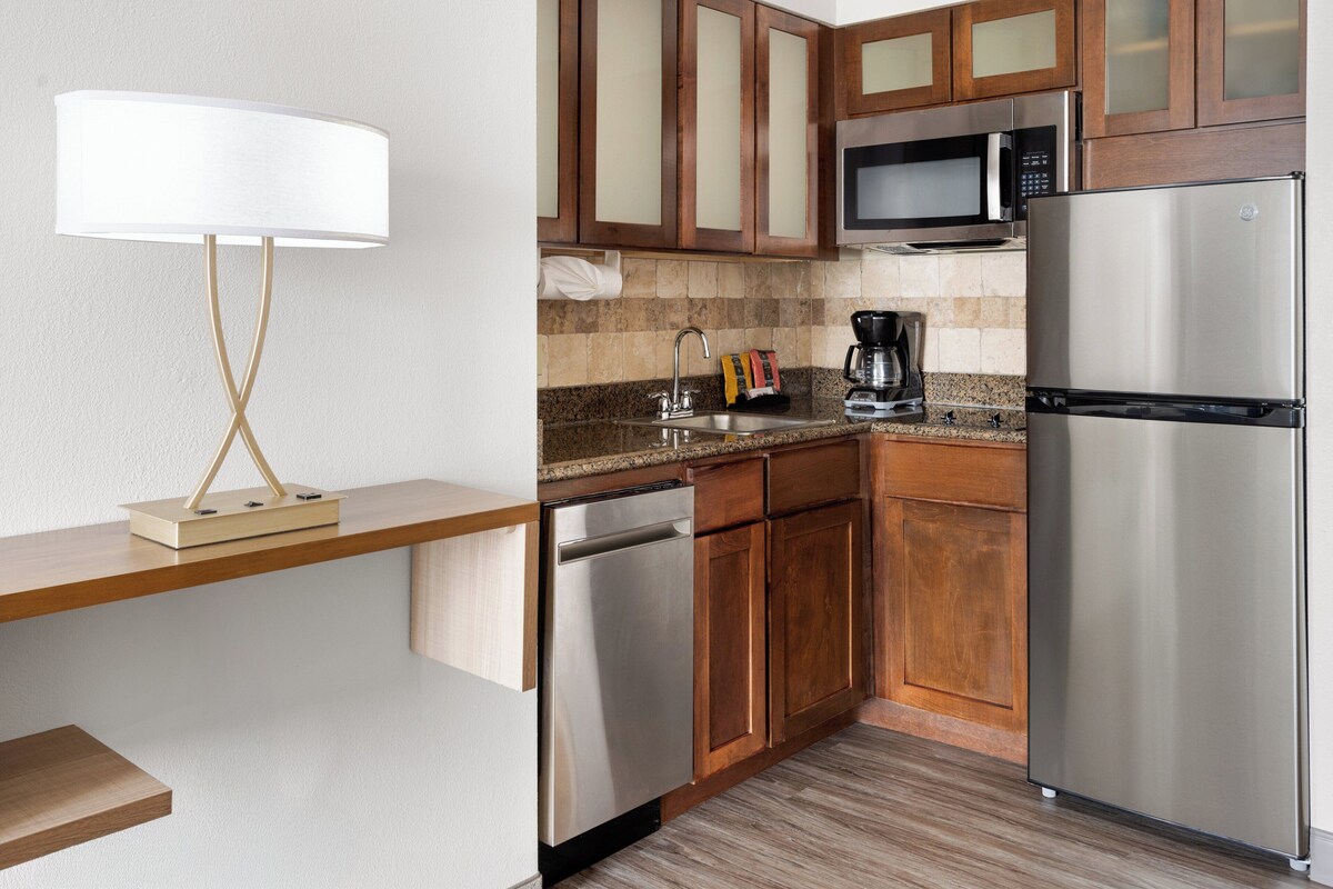 A modern kitchen with wooden cabinets, stainless steel appliances, a built-in microwave, and a coffee maker.