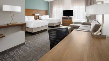 A hotel room with two beds, a TV, a desk with a lamp, a chair, and a large wooden table.