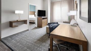 Une chambre d’hôtel équipée d’un lit, d’un bureau, d’une chaise, d’une télévision, d’une lampe et d’une fenêtre avec des rideaux.