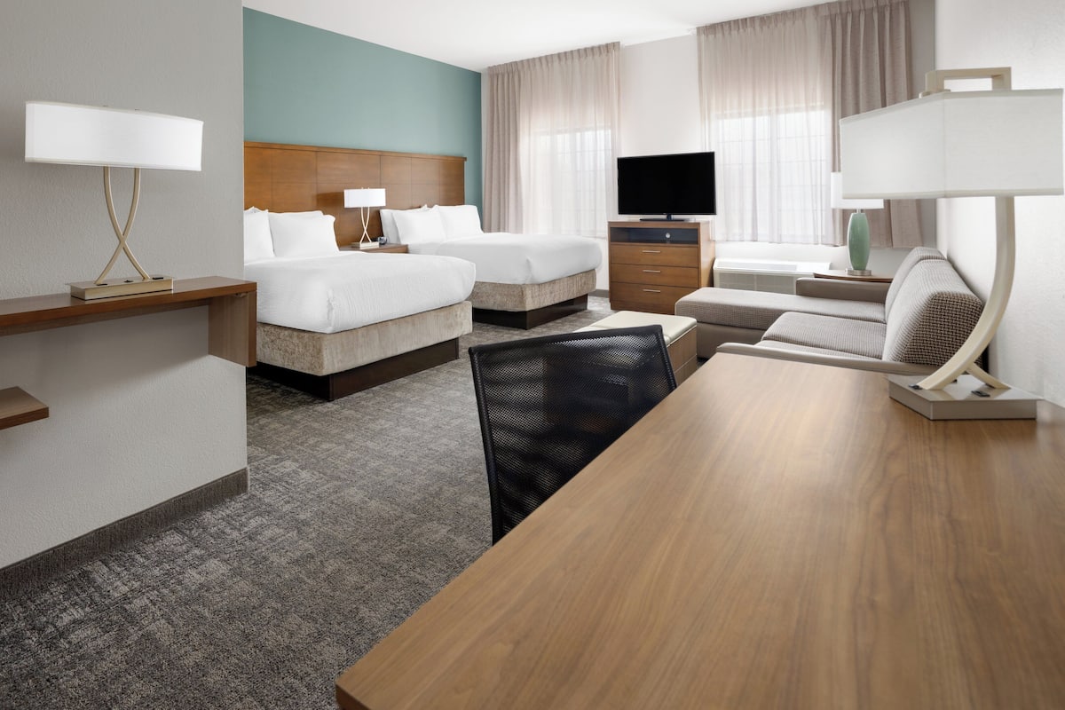 Een hotelkamer met twee bedden, een televisie, een bureau met lamp, een stoel en een grote houten tafel.