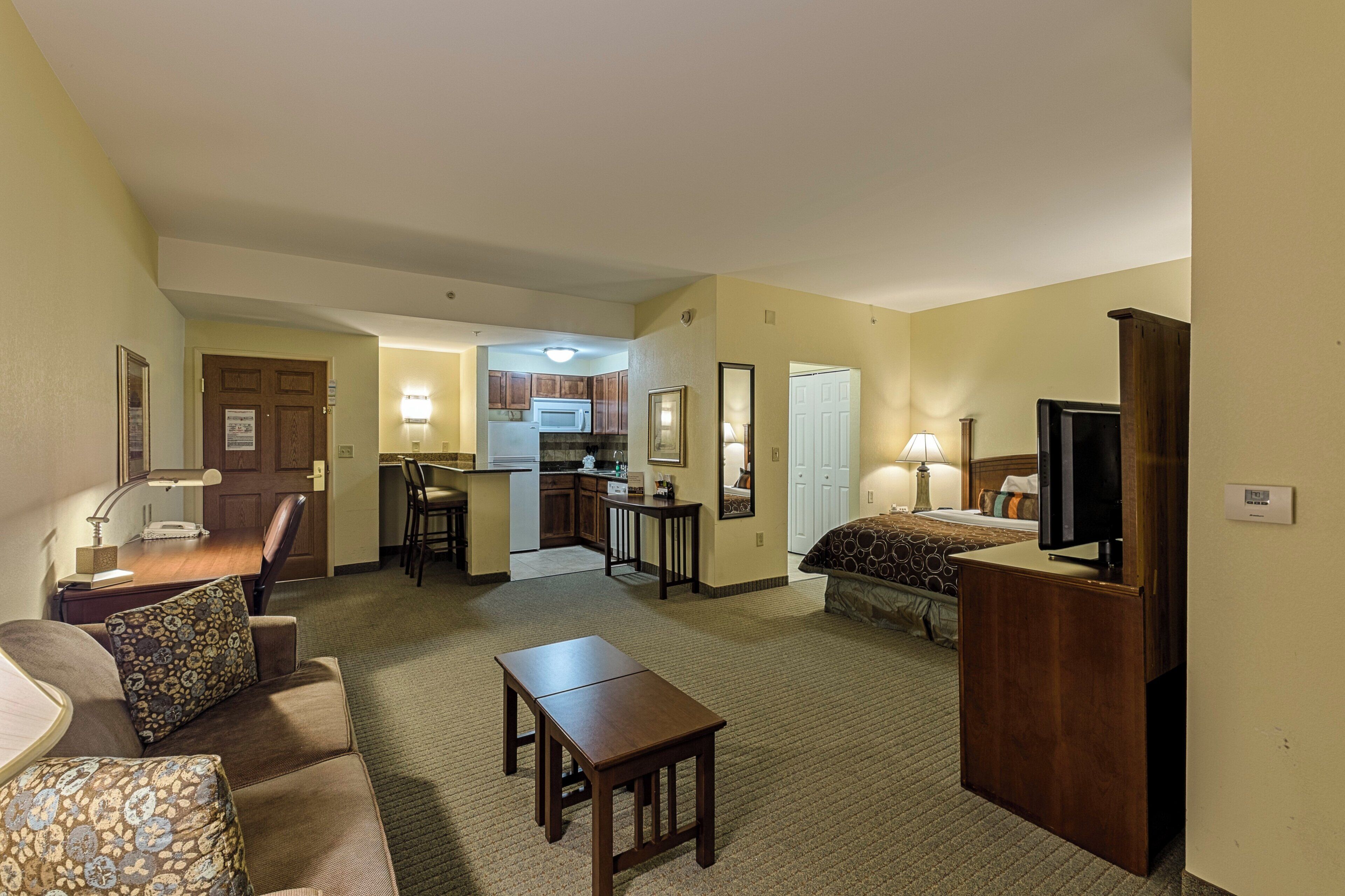 A hotel room with a bed, a desk, a chair, a television, and a kitchenette.