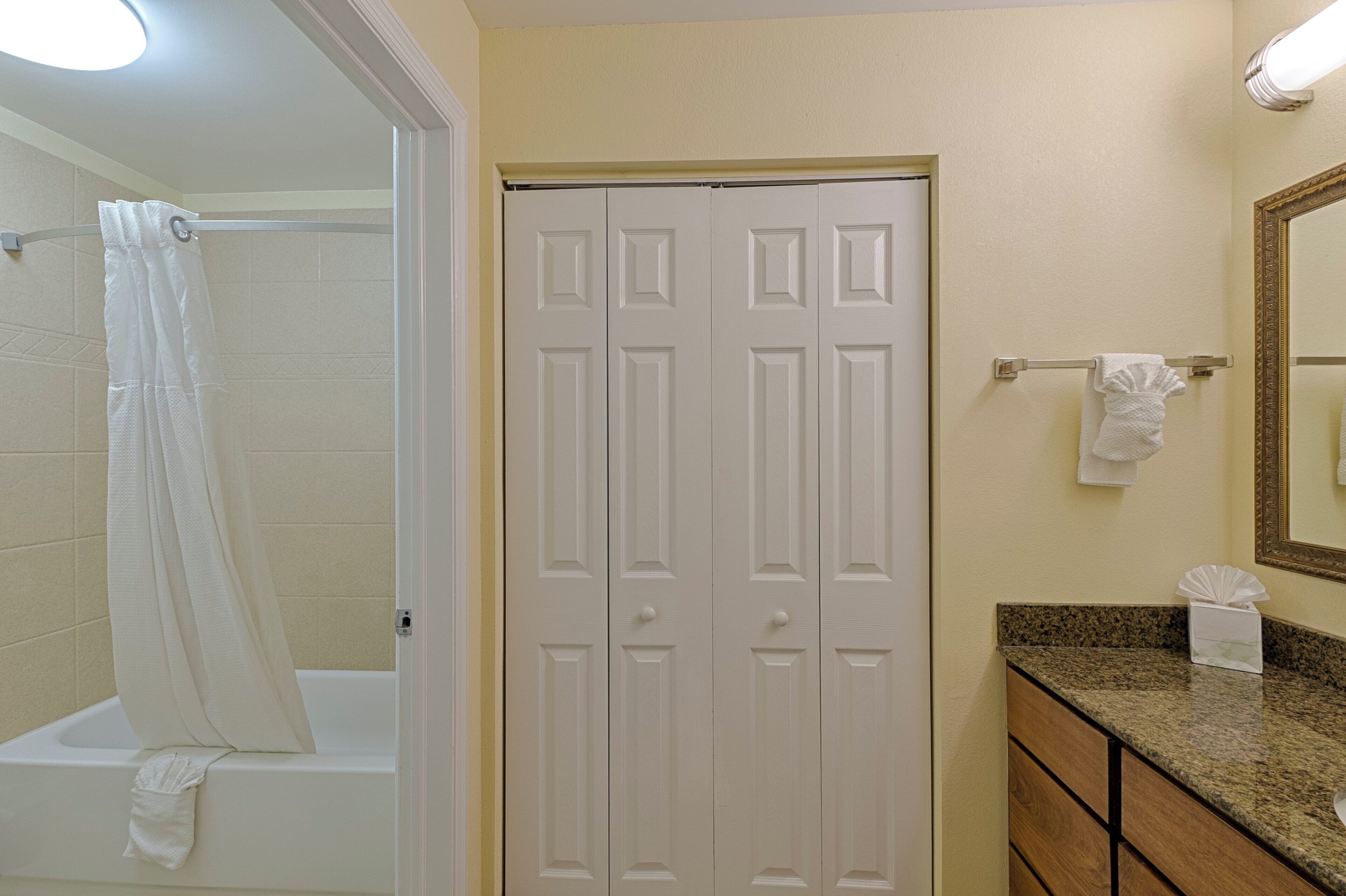 A bathroom with a shower, a toilet, a sink with a mirror, and a door.