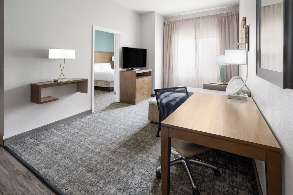 Een hotelkamer met een bed, een bureau, een stoel, een televisie, een lamp en een raam met gordijnen.