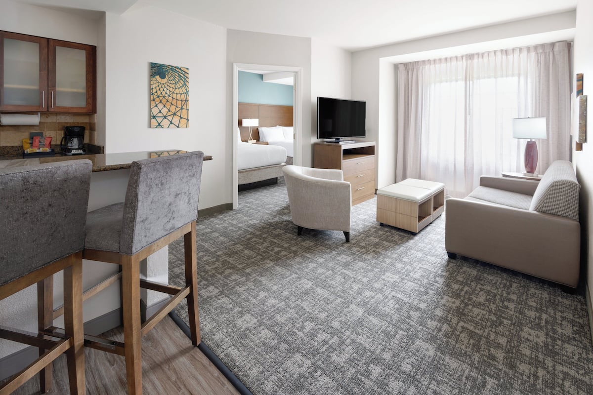 Een hotelkamer met een kitchenette, een bed, een televisie, een bank en een bureau.