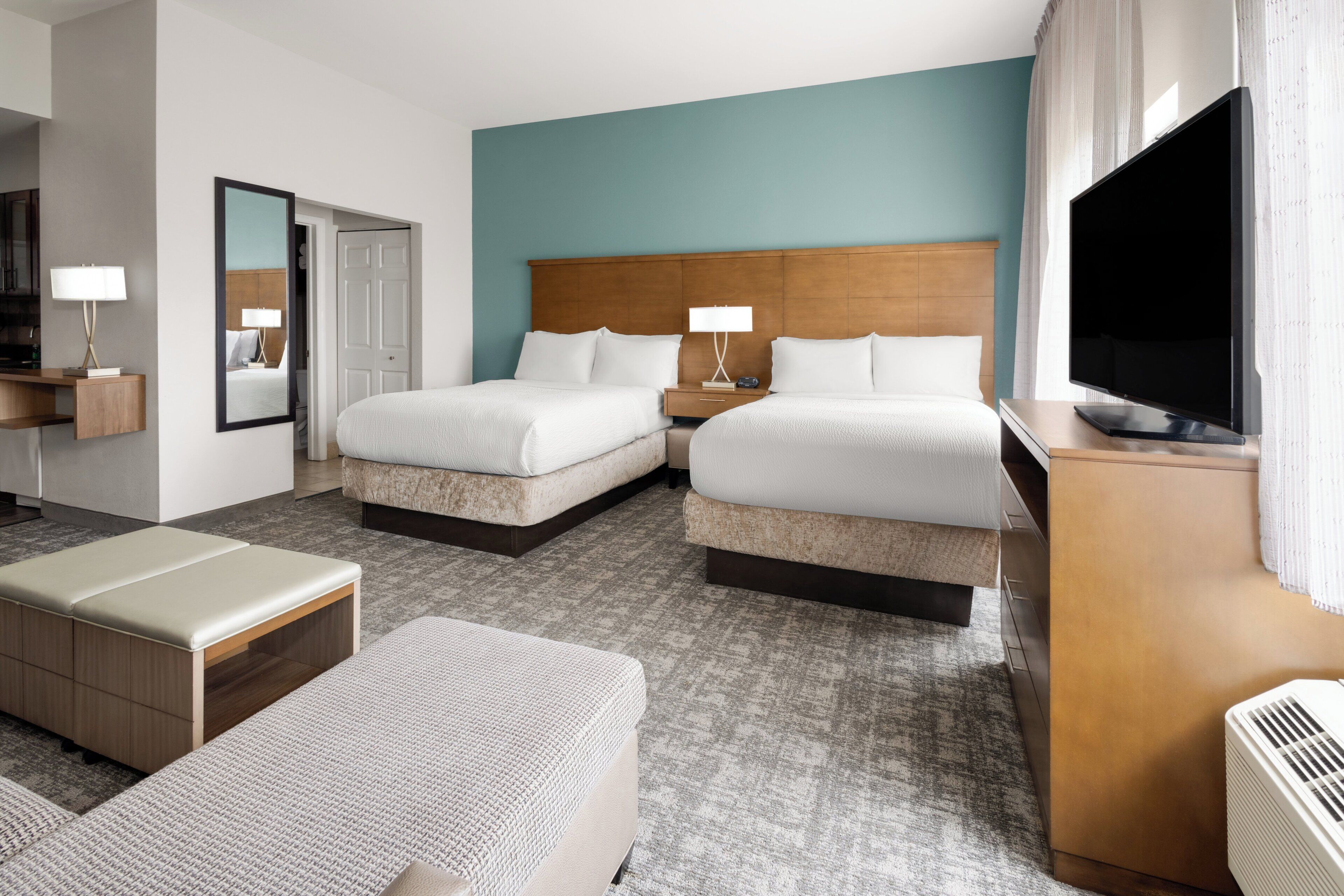 Quarto de hotel com duas camas, uma escrivaninha, televisão e espelho.