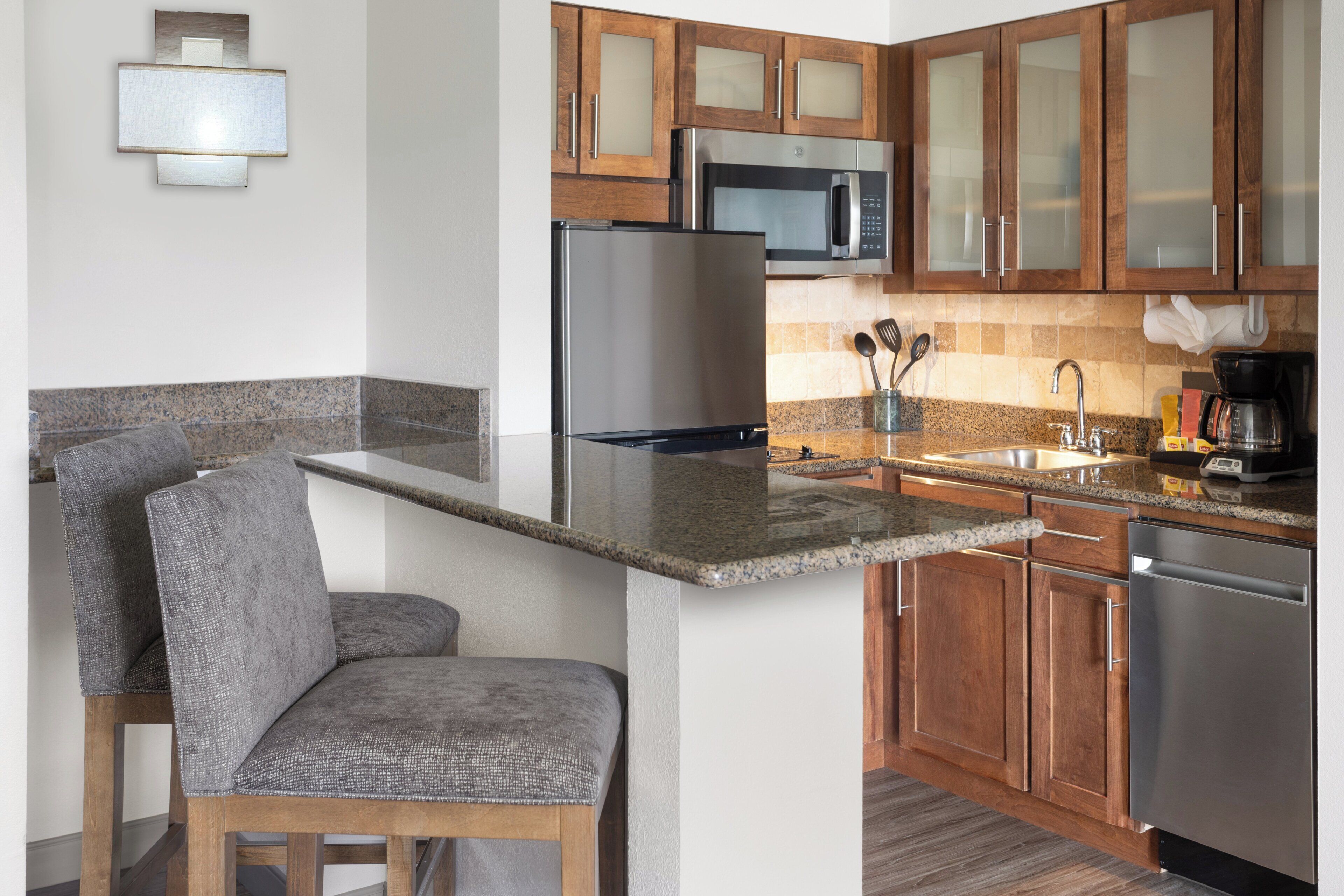 A modern kitchen with granite countertops, stainless steel appliances, wooden cabinets, and a bar area with a cushioned bench.