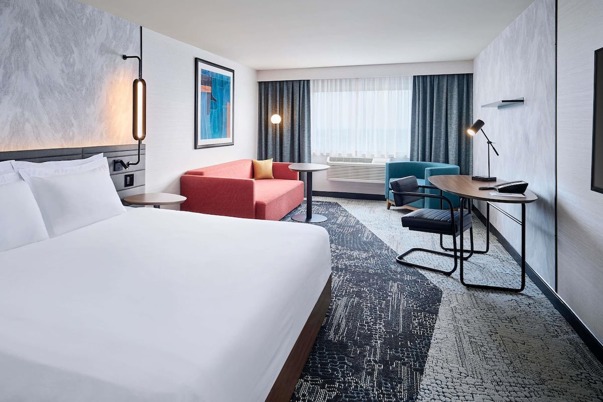 Una habitación de hotel con una cama grande, un sofá rojo, una mesita de noche con una lámpara y un escritorio con una silla.