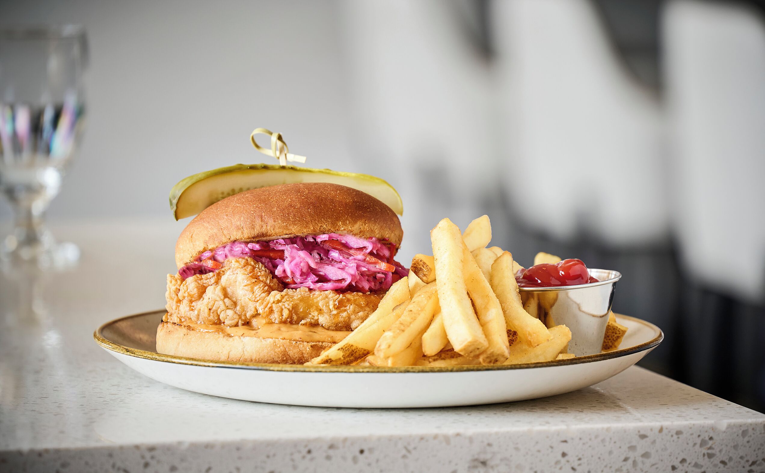 Een bord met een gefrituurde kip sandwich, frietjes en een klein bakje ketchup.