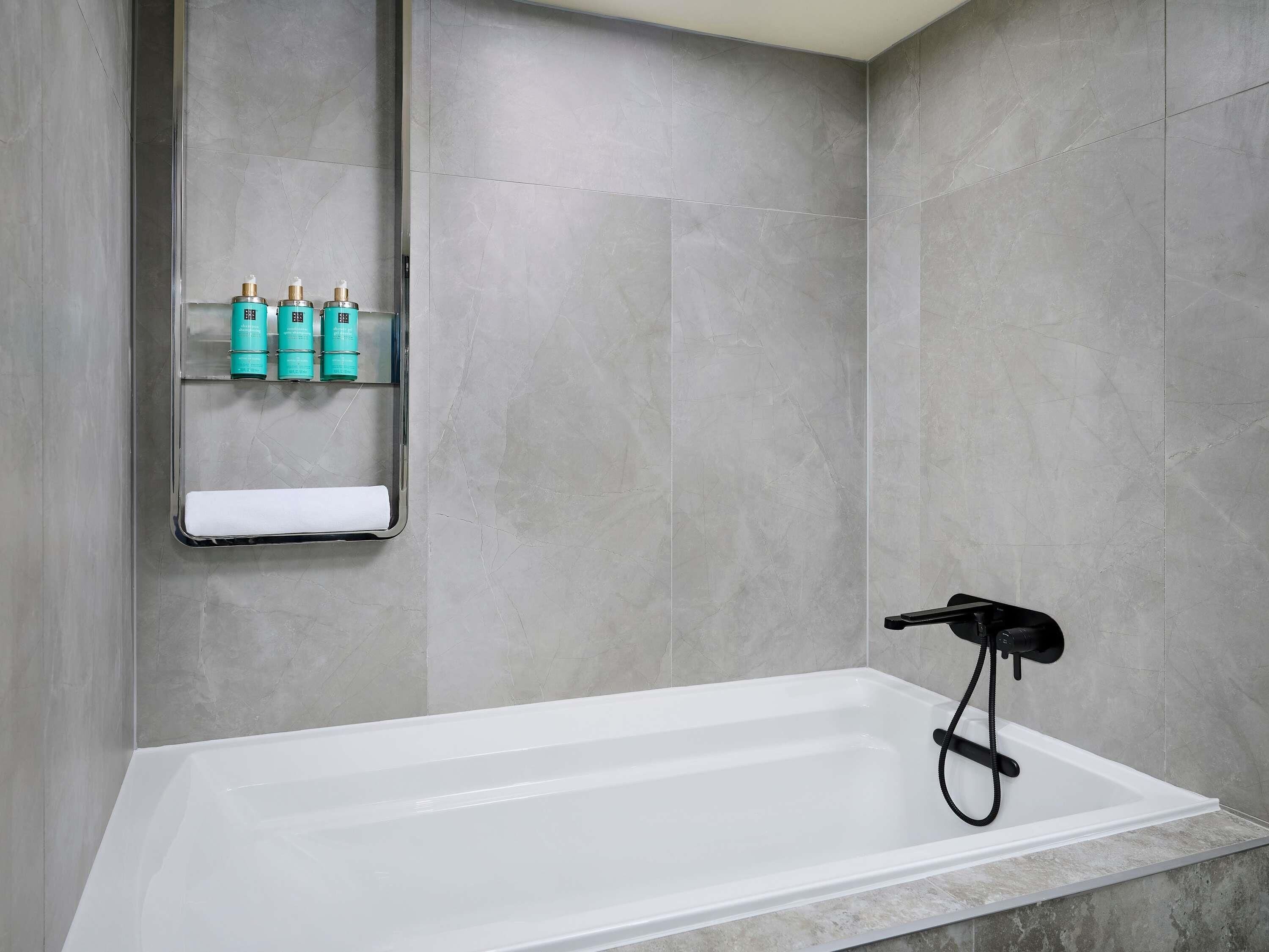A modern bathroom with a white bathtub, a towel rack with bottles, and a black showerhead.
