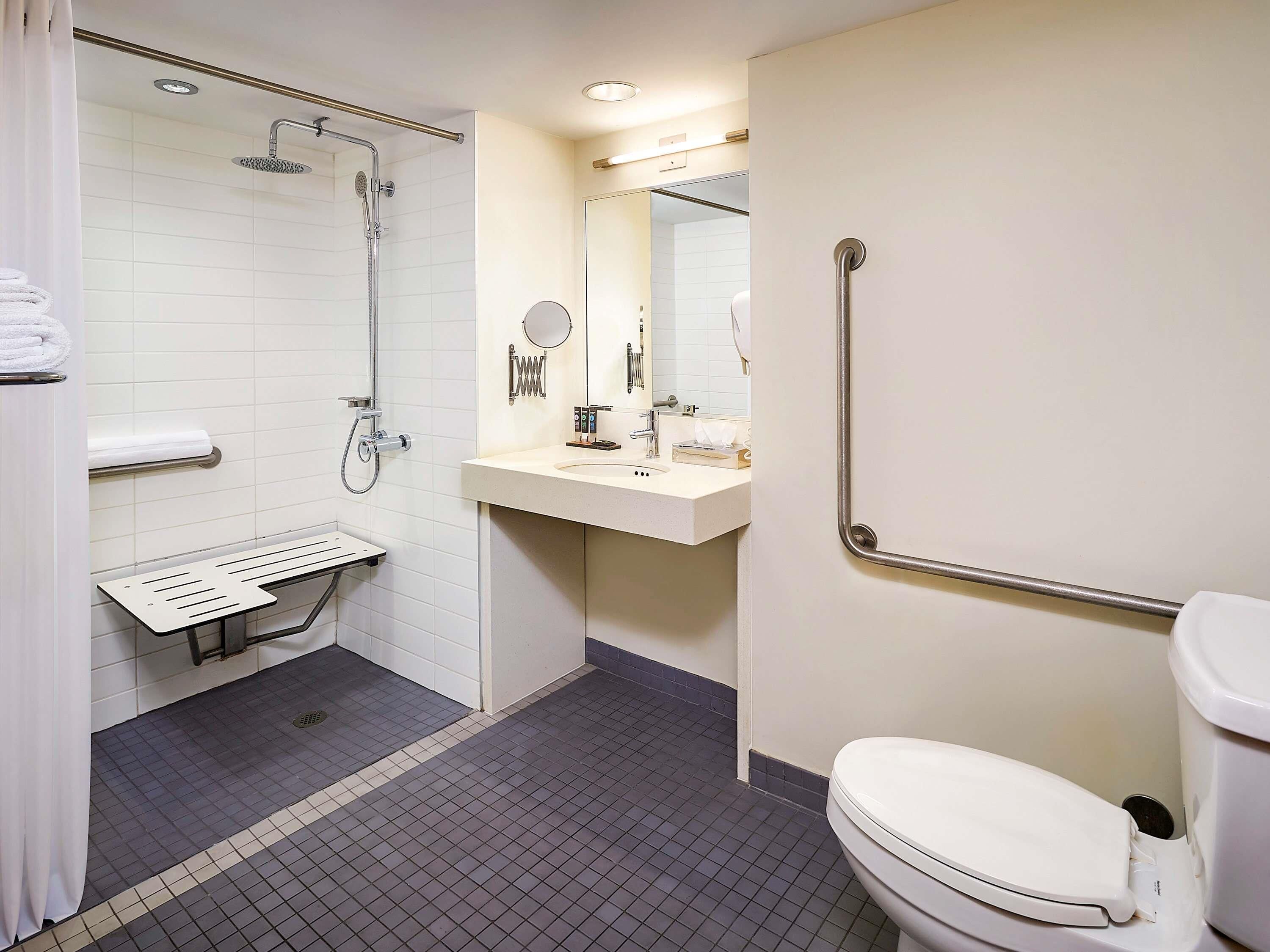 Un baño moderno con ducha, inodoro, lavamanos y barras de apoyo.
