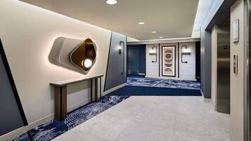 Un pasillo moderno de hotel con alfombra azul, iluminación empotrada y un panel informativo en la pared.