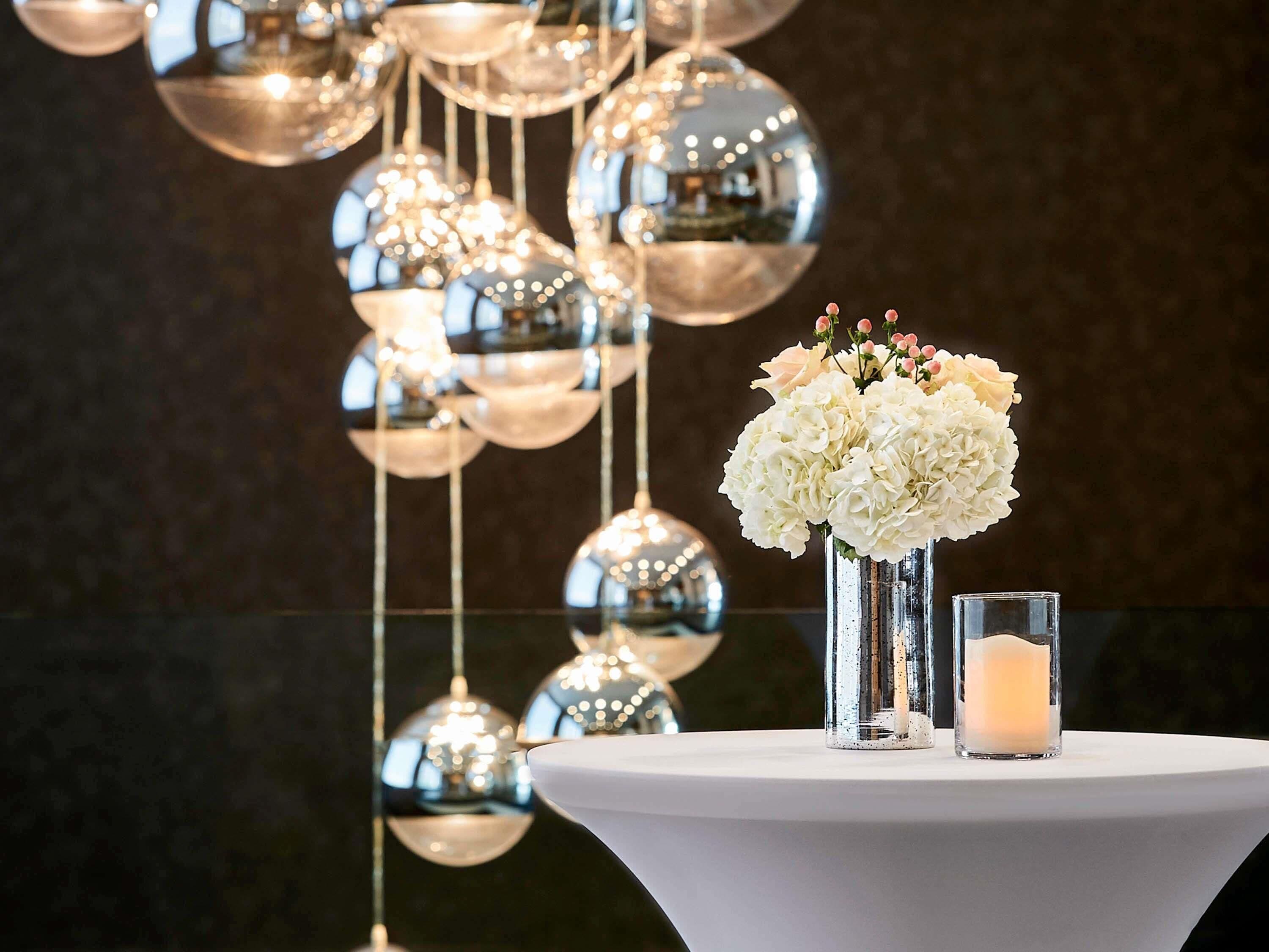 A table with a white tablecloth, a glass vase with white flowers, and a lit candle.
