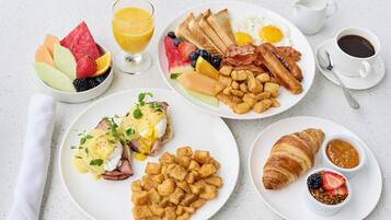 A breakfast spread with toast, eggs, bacon, sausages, hash browns, fruit, and a croissant.