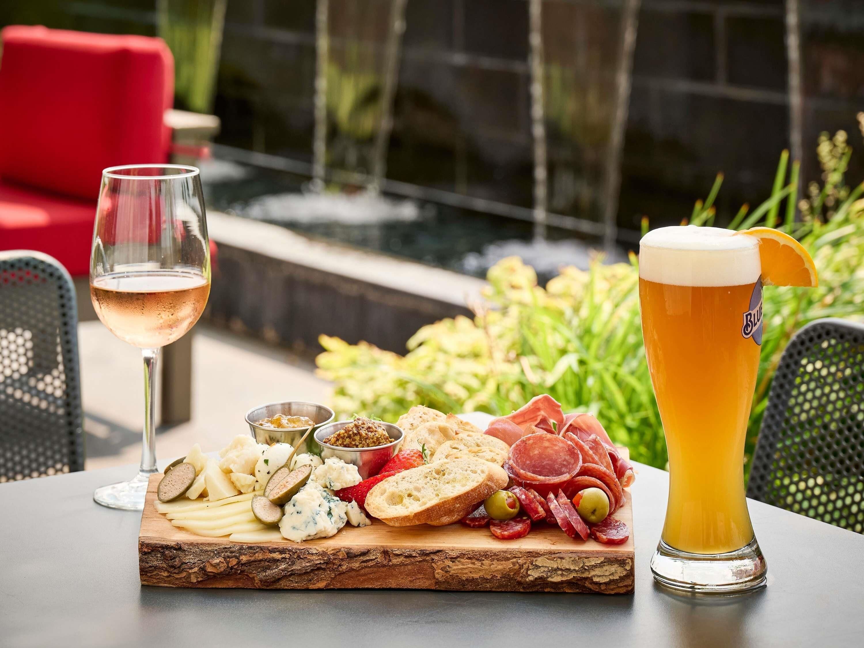 A table with a variety of cheeses, meats, and bread, accompanied by a glass of beer and a glass of wine.