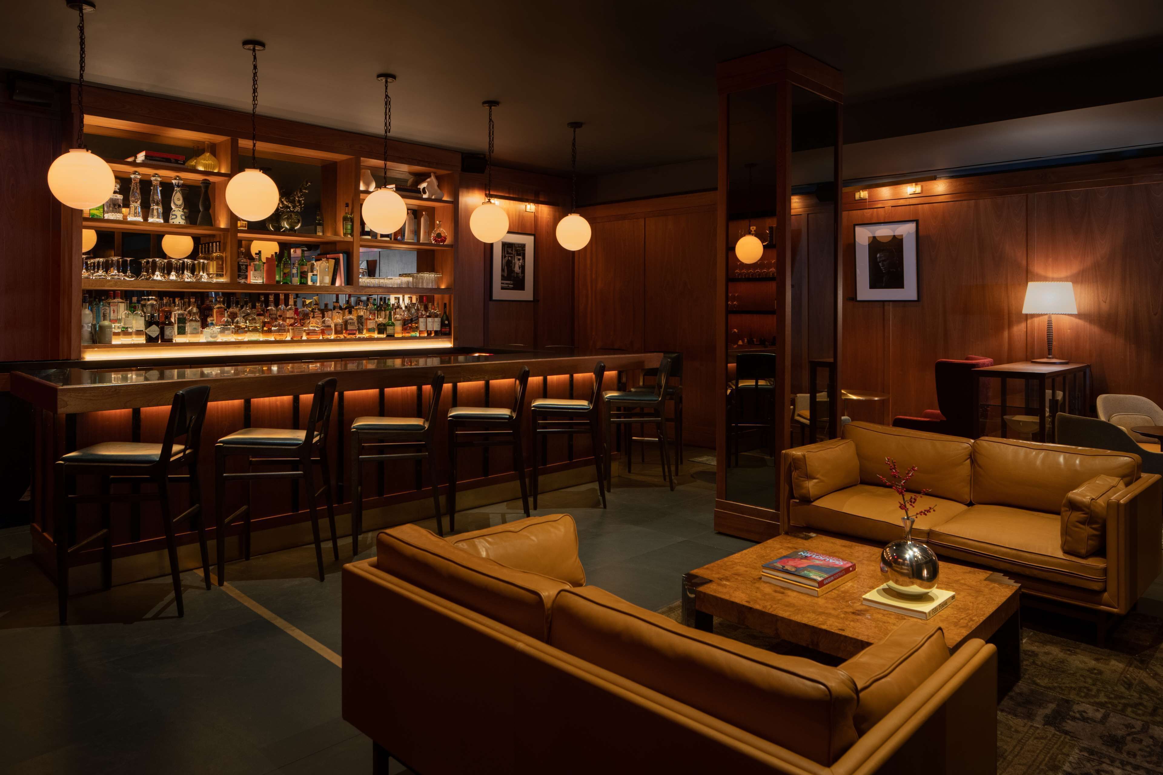 Uma área de bar com prateleiras de madeira, luminárias pendentes e assentos de couro.