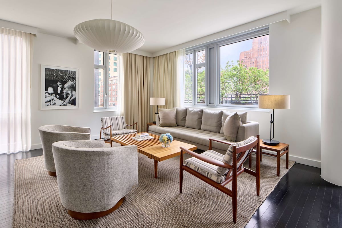 A modern living room with a sofa, armchairs, a coffee table, and a large window offering a city view.