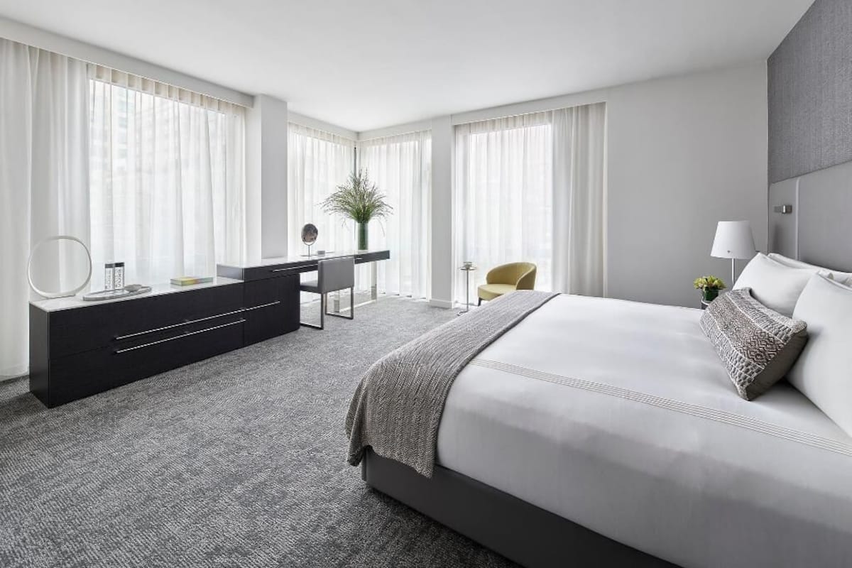 A modern hotel room with a large bed, a desk, a chair, and a dresser.