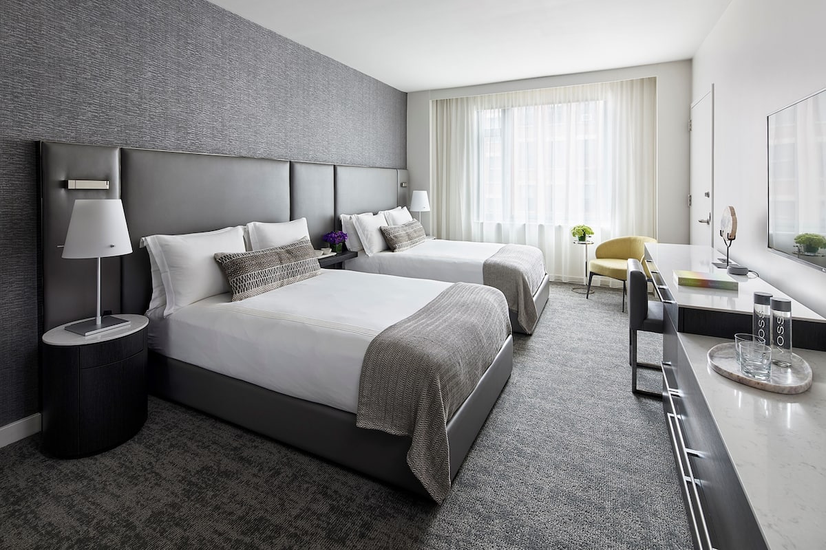 A modern hotel room with two beds, a desk, and a chair.