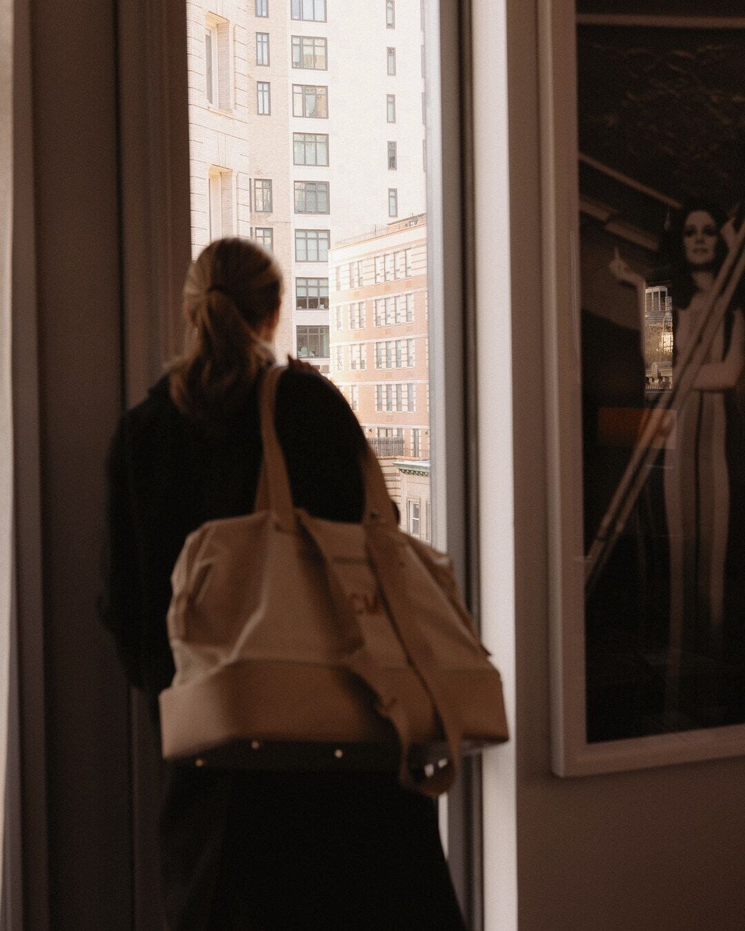 Una persona de pie junto a una ventana con vistas a un edificio.